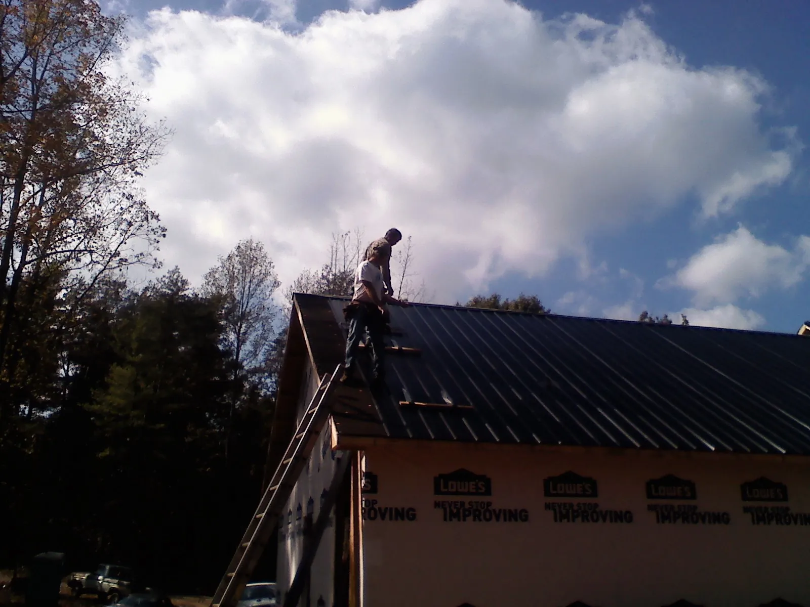 Roofer fastening dark metal panels high against a cloudy sky, from a Roof Inspection job in Elmhurst