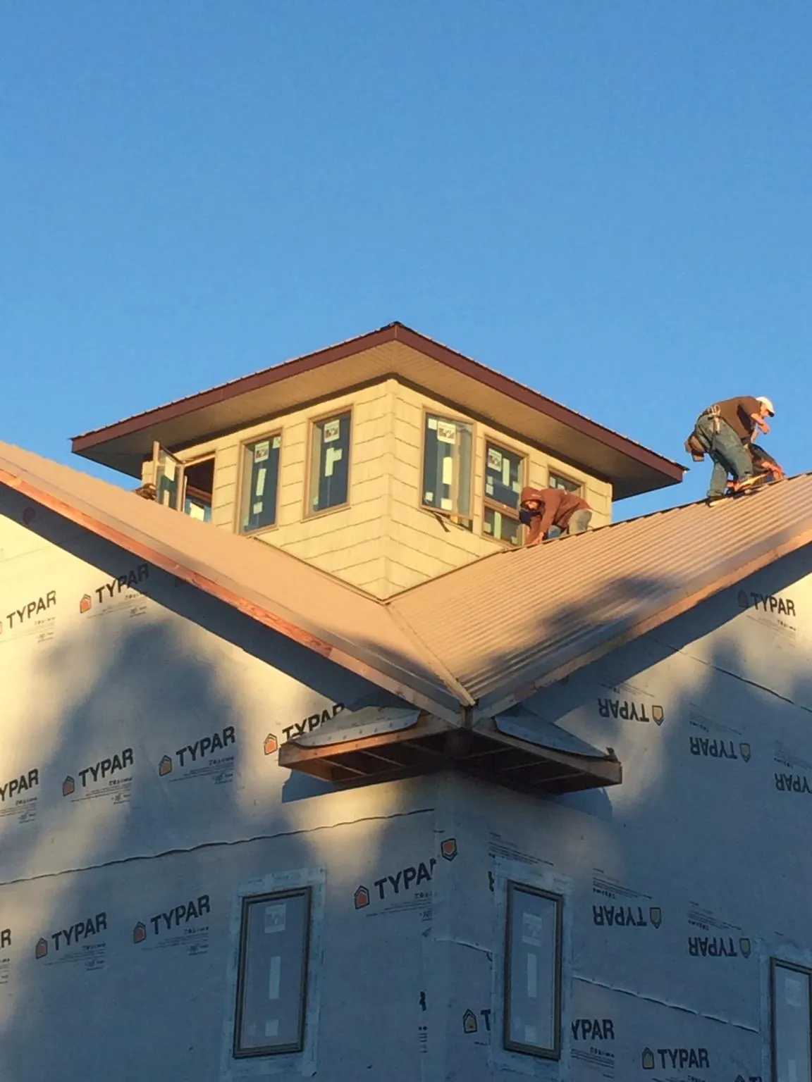 Roofers working around a rooftop cupola on a new metal roof at sunset — Roof Waterproofing in Elmhurst by Roofing Brothers